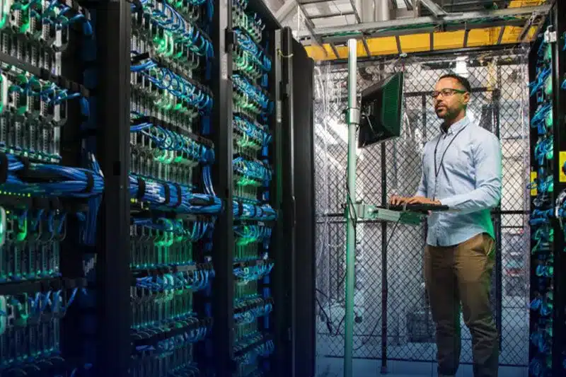 Technicien supervisant le câblage informatique dans une salle de serveurs, utilisant un ordinateur pour gérer l'infrastructure réseau.