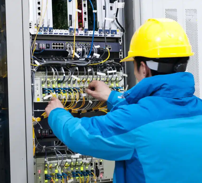 Technicien de câblage réseau effectuant des connexions dans un panneau de distribution, portant un casque de sécurité.