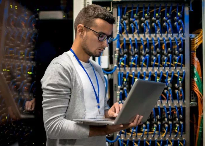 Un technicien installe des câbles à fibre optique dans un centre de données, manipulant des connexions de câblage avec précision.