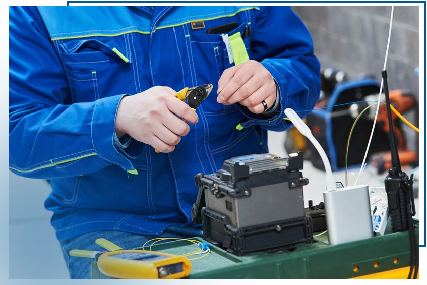 Un technicien en uniforme bleu effectue une installation de câbles à fibre optique à l'aide d'un outil de coupe et d'équipement spécialisé.